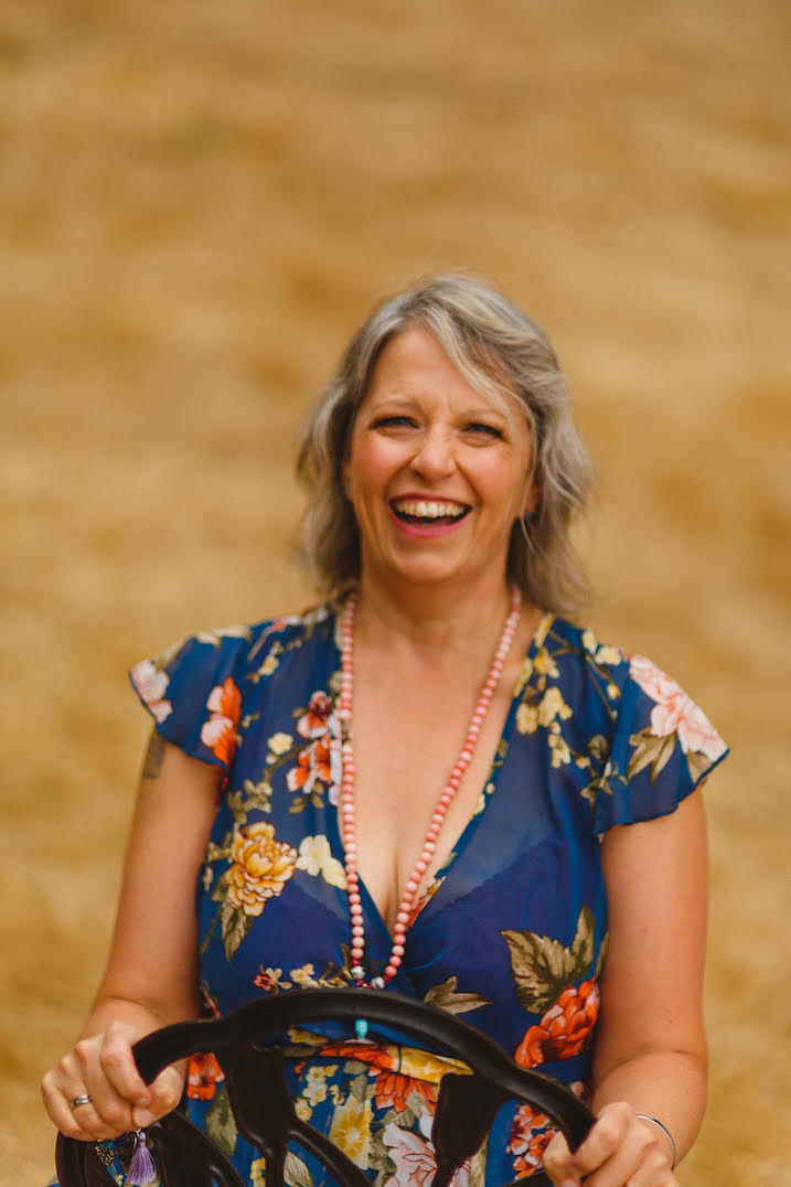 A smiling lady with a large, beautiful, happy smile wearing a blue flowered dress on a blurred beige background