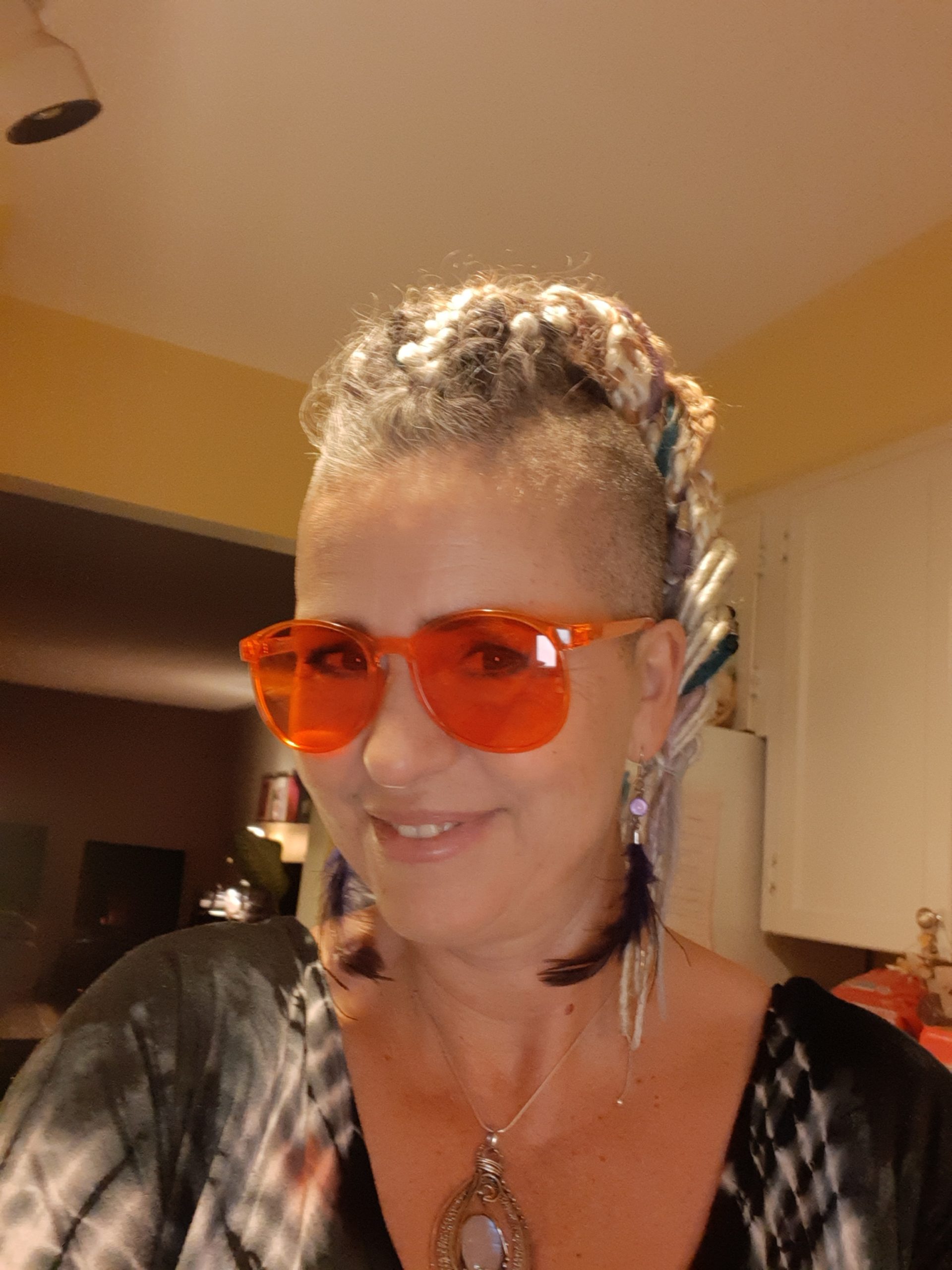 A beautiful smiling blond lady with orange glasses and long feather earrings