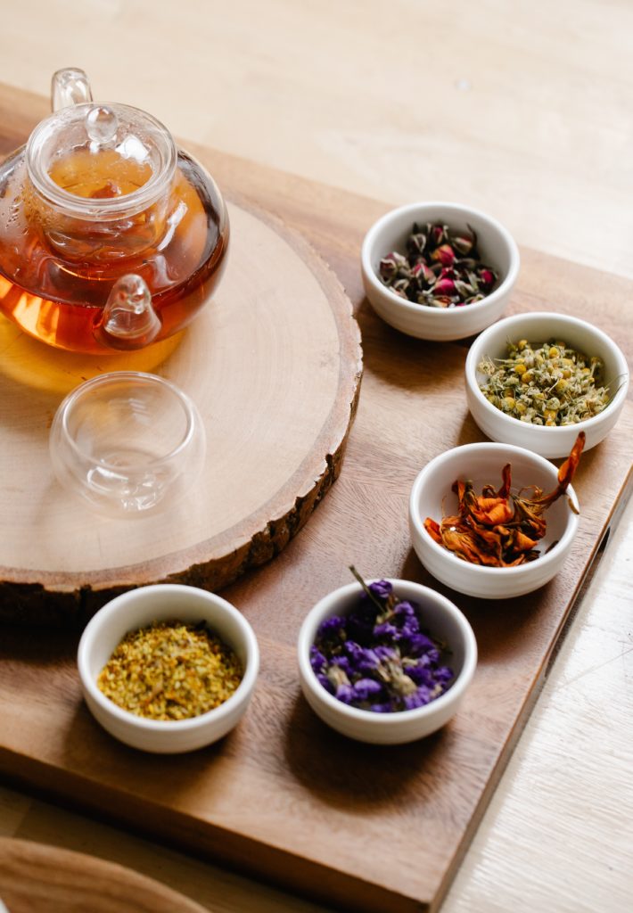 Medicinal herbs in bowls surrounding a teapot of tea and an empty tea glass