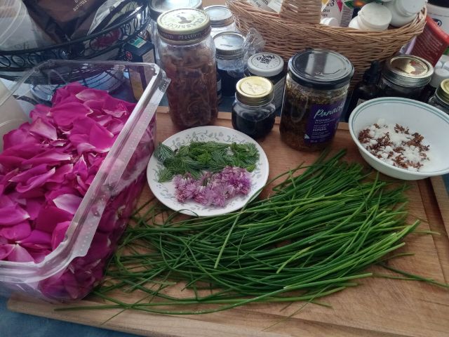 Image of chives and rose petals, surrounded by jars of herbal medicines, tonics, and various herbs